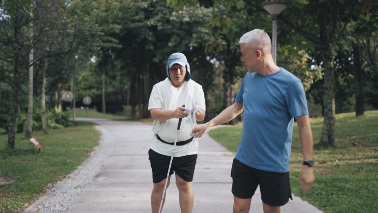 Asian Chinese Guide runner and visually impaired mature man jogging in the park during weekend morning