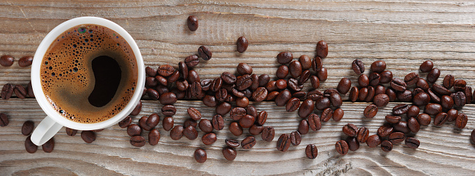 Cup of coffee and roasted beans as line on wooden background, top view