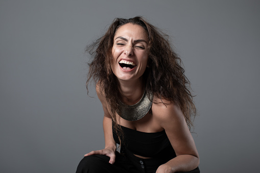 Portrait of a beautiful young woman laughing while sitting against a gray wall.