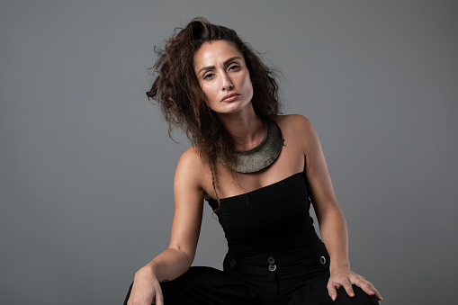 Fashion portrait of elegant woman sitting against gray background.