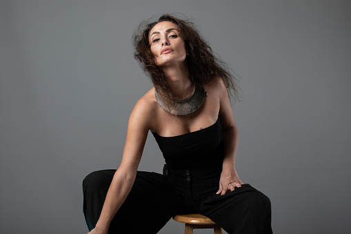Fashion portrait of elegant woman sitting against gray background.