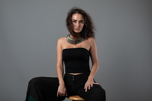 Fashion portrait of elegant woman sitting against gray background.