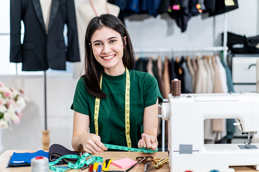 Smiling Caucasian female fashion designer works in studio choosing colorful fabric for a dress design collection and looking at camera , choose clothing colors for tailoring and designing