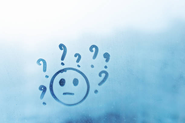 Doodle cheerless smile face with question marks around head painted on blue window flooded with raindrops on blur glass background in city, concept photo