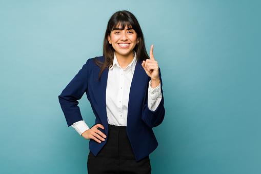 Attractive hispanic woman showing her finger saying the number one business while loving her work next to copy space