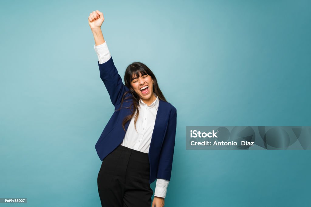 Excited professional woman looking confident Hispanic young woman raising her arm and celebrating her successful business while working wearing a professional suit Businesswoman Stock Photo