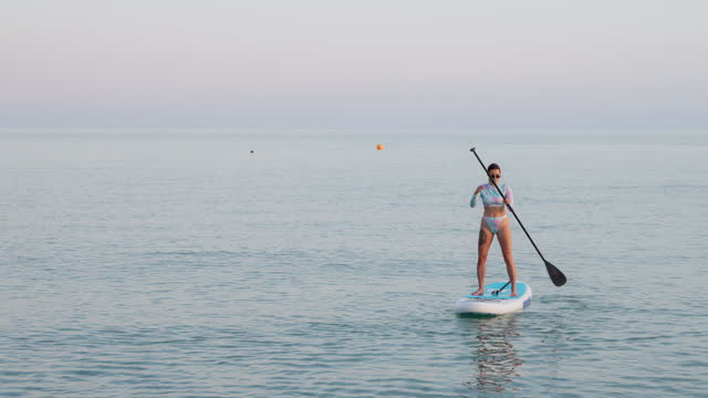 SUP surfing and SUP touring on sea, beautiful young woman is standing on board and paddling