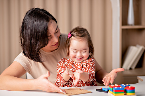 child with down syndrome with educational toys smiles, a cute girl with her mother a teacher