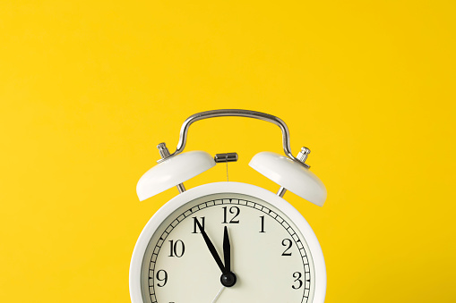 Retro style alarm clock on yellow background.