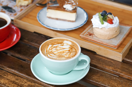 A cup of cappuccino with mini pavlova and a slice of biscoff cheese cake on a wooden tray. Selective focus.