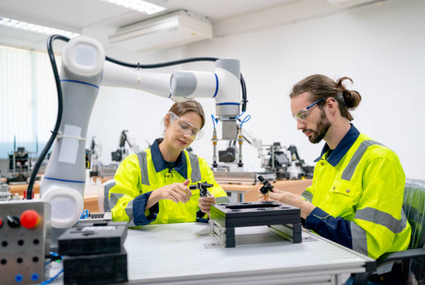istock Two Caucasian professional technician or engineer workers sit in workplace and help to check and work with quality control the robotic arm machine in factory together and look happy during work. 1469487358