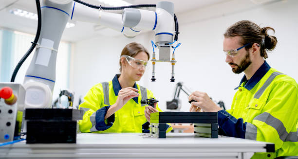 istock Two Caucasian professional technician or engineer workers sit in workplace and help to check and work with quality control the robotic arm machine in factory together and look happy during work. 1469487379