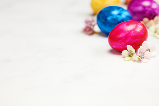 Easter eggs painted in pastel colors on a white background with copy space and cute spring flowers, Happy Easter Holiday concept with space for text. Yellow pink and blue bright colors