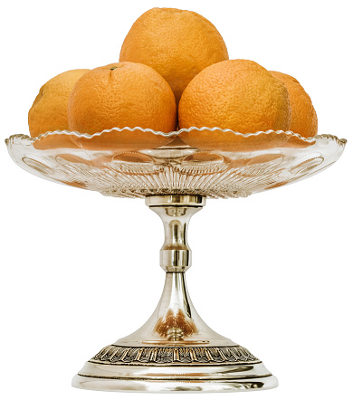 Studio shot of bunch of Oranges set in vintage glass cake stand plate with embellished patinated silver pedestal, isolated on white background, side view.