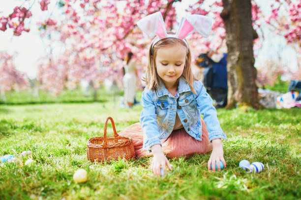 девочка-дошкольник в ушах кролика играет в охоту за яйцами на пасху - child discovery surprise playing стоковые фото и изображения