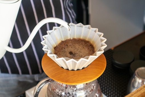 Close-up view of pouring hot water into a paper coffee filter while the coffee is boiling