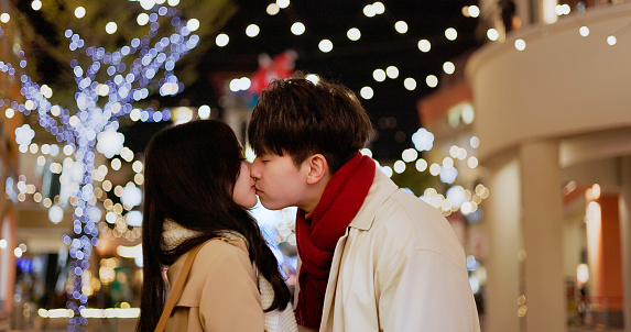 asian dating couple wearing scarves are embracing each other and kissing affectionately on street