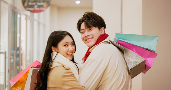 asian dating couple wearing scarves are window shopping and turning around - smiling at you