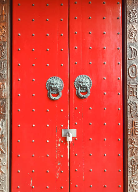 Red door with lion heads door knobs. Old red wooden chinese gates with symbols on door frame.
