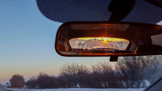 Winter sunset in car rear view mirror while driving