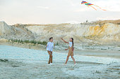 A boy and a girl launch a bright kite standing on the edge of a mountain near a pond