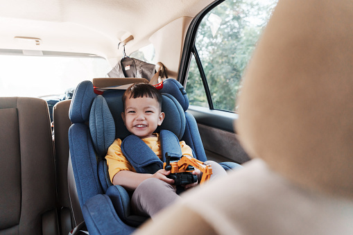 Cheerful smiling Asian little boy in safety car seat, Happy small child travel by car with family.