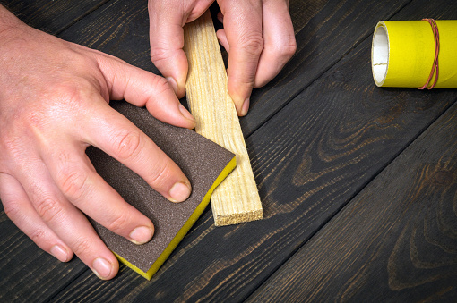 The master polishes a wooden board with an abrasive tool