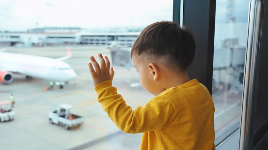 Cute Little Asian little child boy looking out of terminal window for Arriving and Departing Airplanes, Little Chinese passenger traveler waiting for his Flight.