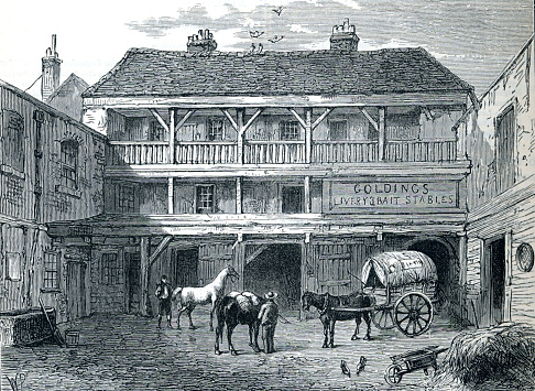 Building showing Goldings Livery Stables Horses One attached to a wagon In foreground straw and wheelbarrow