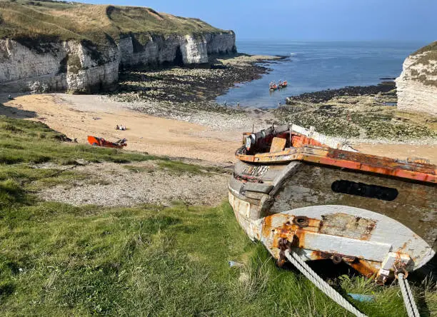 North Landing beach and Flamborough Cliffs at low tide on a sunny summer's day. A disused wooden fishing boat in the foreground with two boats heading out to sea in the distance. East Riding of Yorkshire, England, UK.
