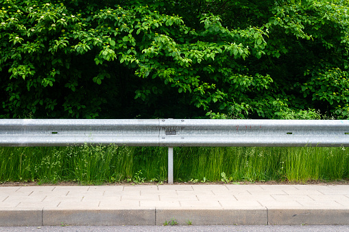 Sidewalk, highway guard rail, green grass and bushes. Background for copy space.