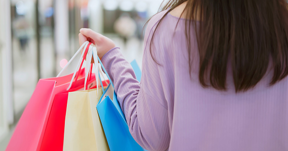 rear view hand close up asian woman hand hold colorful shopping bags walking in department store or mall - shopaholic concept