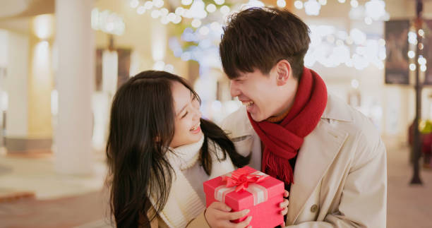 Happy couple opening a colorful polka dot gift box outdoors, enjoying a surprise moment together