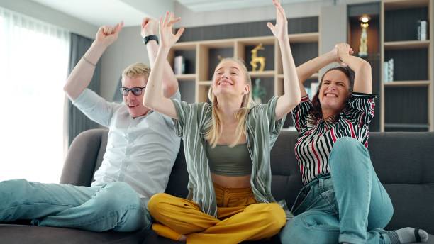 cheerful happy caucasian family cheering for favorite team and it scoring goal and winning game. mother, father and daughter watching tv with sports celebration cheers, hands holding up - soccer celebration success group of people imagens e fotografias de stock