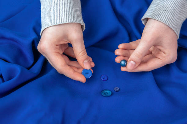 the girl selects buttons matching the color of the blue fabric. hobby, sewing. - article textile material new imagens e fotografias de stock