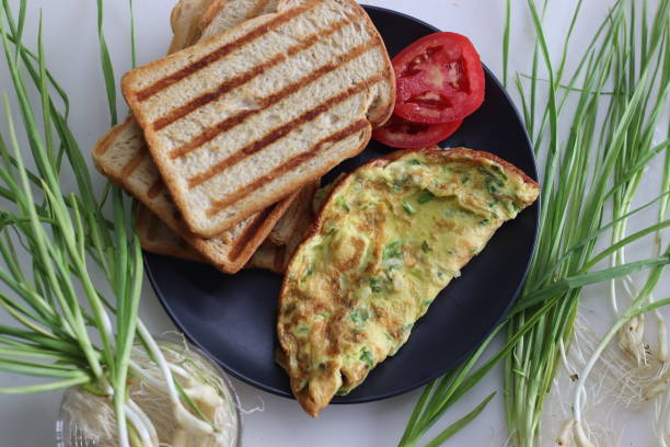 Egg omelette with finely chopped green garlic, green chillies served with butter toasted bread and fresh tomatoes Egg omelette with finely chopped green garlic, green chillies served with butter toasted bread and fresh tomatoes. Shot on white background. finely stock pictures, royalty-free photos & images