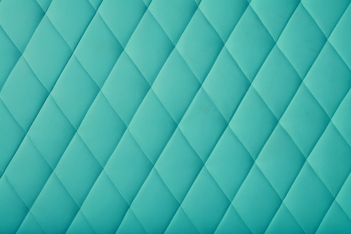 Background texture of teal blue leather soft tufted furniture or wall panel upholstery with deep diamond pattern, close up