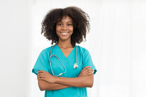 retrato de jovem médica sorridente ou jovem enfermeira vestindo uniforme de esfoliação azul e estetoscópio e de pé com os braços cruzados enquanto olhava para a câmera isolada no fundo branco - nurse scrubs isolated doctor - fotografias e filmes do acervo