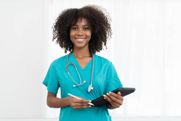 retrato do médico jovem sorridente ou da enfermeira jovem vestindo uniforme e estetoscópio de esfoliação azul e de pé segurando o comprimido isolado no fundo branco - nurse scrubs isolated doctor - fotografias e filmes do acervo