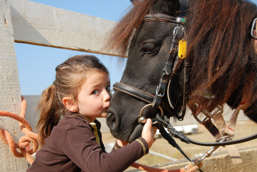 Little girl sitting on a horse backwards, taking a rest after riding, hugging him.