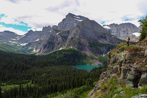 A woman hikes alone along the Grinnel Glacier Trail and a cliffside overlook in Glacier National Park