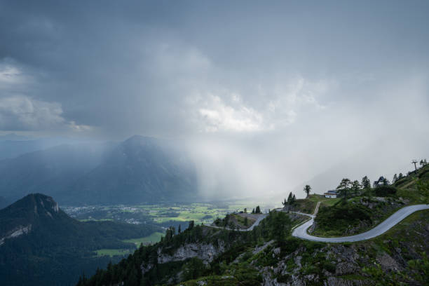 View from high up in the mountains with winding road, partly sunshine down in the valley many clouds above and some rain, showing how fast the weather can change