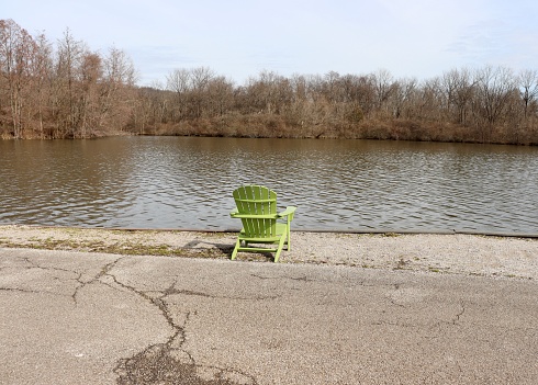 The empty green wood chair overlooking the lake in the park on a sunny day,
