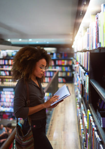 jeune femme afro-brésilienne debout regardant un livre dans une librairie d’ipanema - library young adult bookstore people photos et images de collection