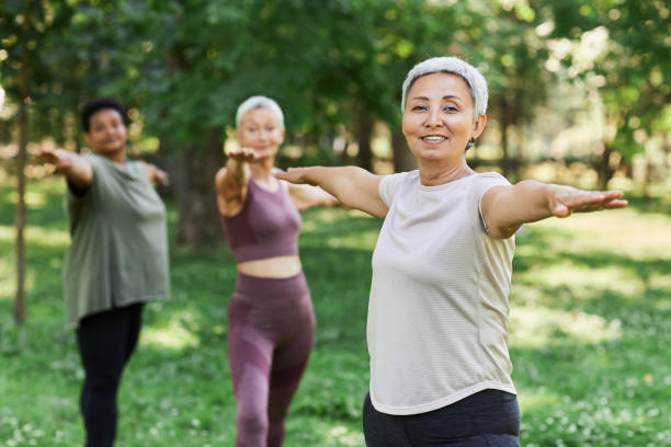 lächelnde ältere frau, die sport im freien trainiert und in die kamera schaut - yoga exercising outdoors group of people stock-fotos und bilder