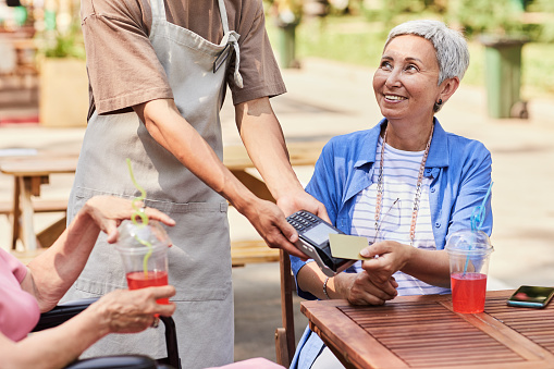 Portrait of smiling senior woman paying to waiter in outdoor cafe