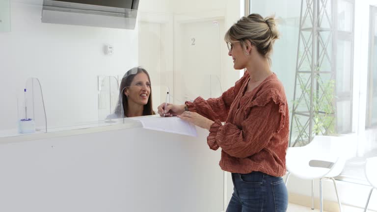 Female patient and female receptionist filling papers and taking