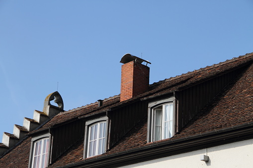 broken and deteriorating grunge old brick meat smoker chimney. cracked mortar joints and loose bricks. clear blue sky. low angle view. weathered concrete tile sloped barn roof. black sooth deposit.