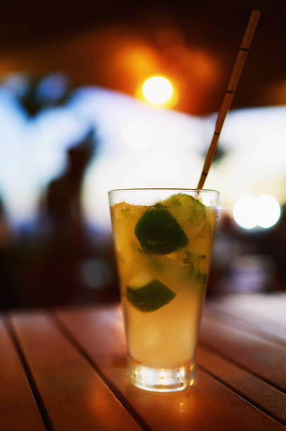 glass cup with cold caipirinha and straw on a wooden table in a bar at sunset on the beach of ipanema - caipiroska imagens e fotografias de stock