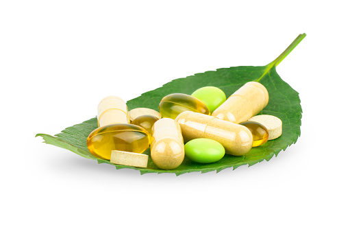 Vitamin, dietary supplement and herbal pills on green leaf isolated on white background, healthcare concept